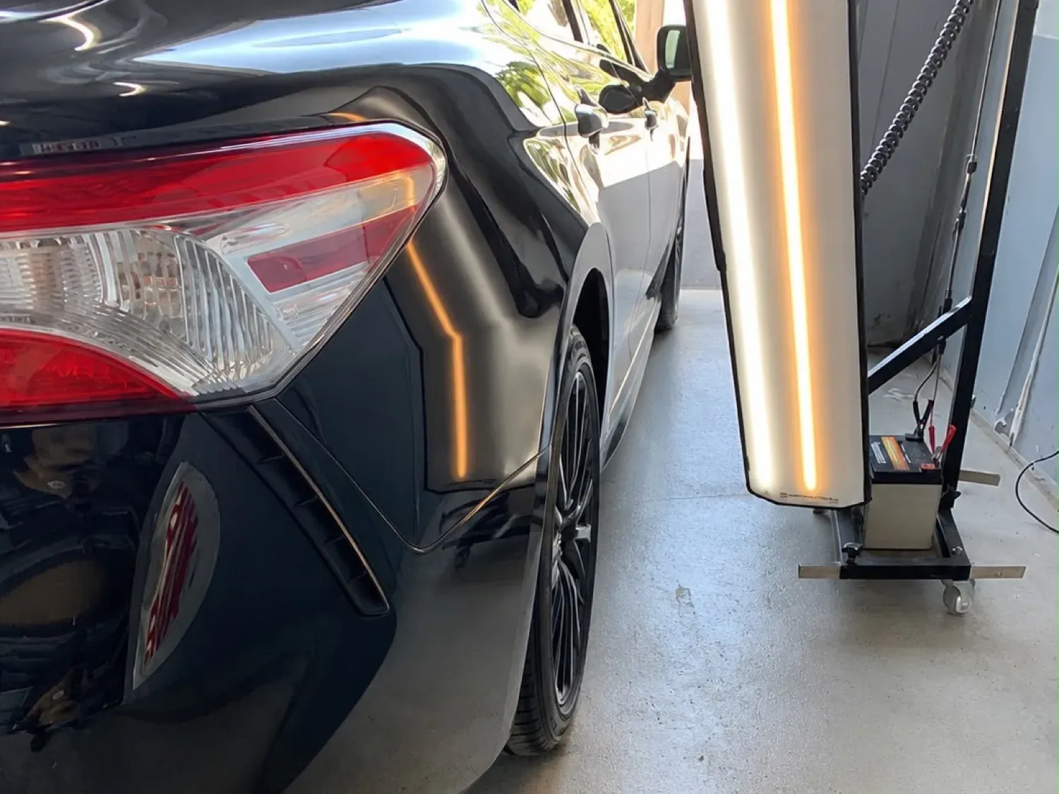 Dent in the rear quarter of a black car under a PDR light, before and after — after