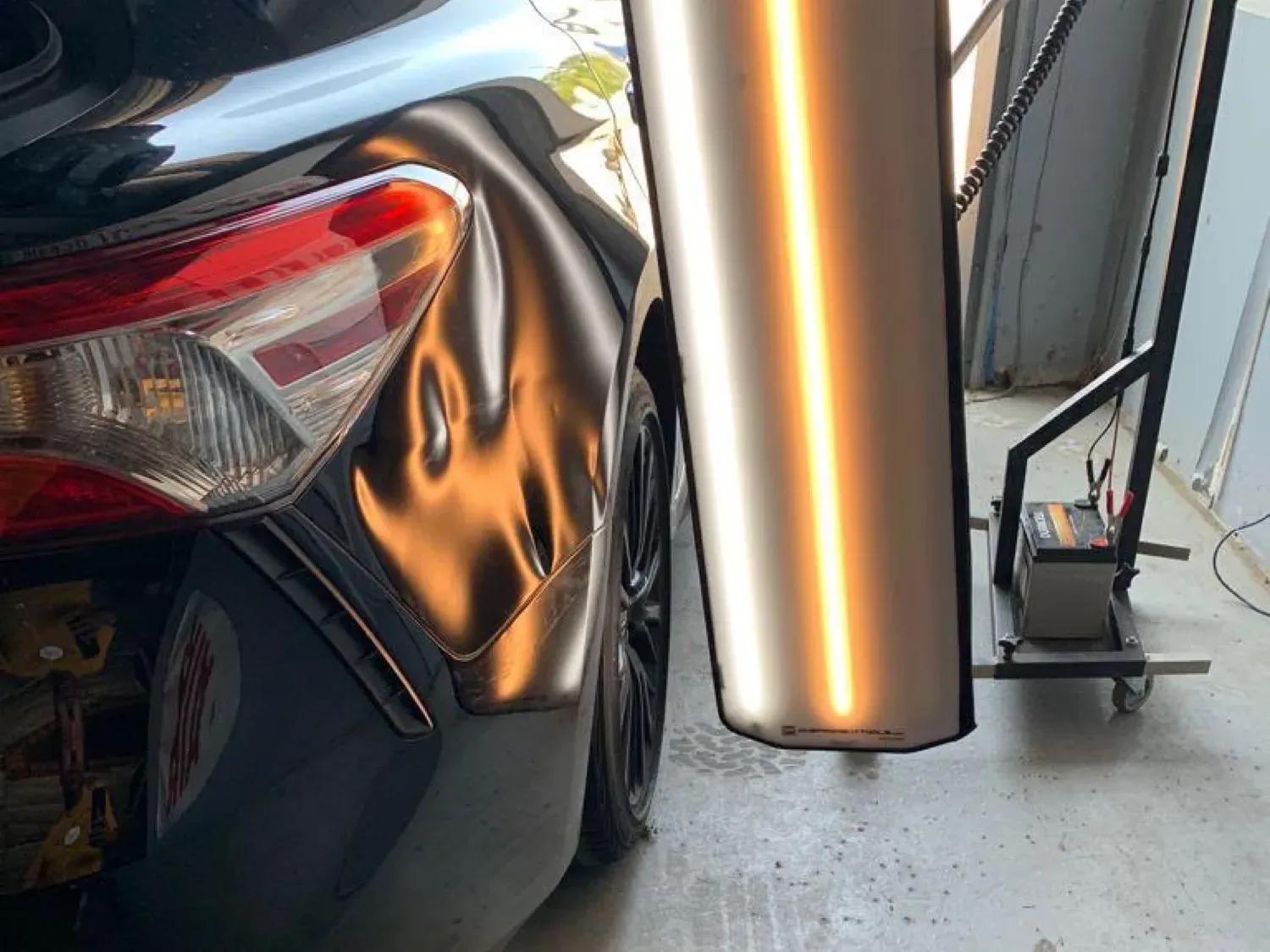 Dent in the rear quarter of a black car under a PDR light, before and after — before