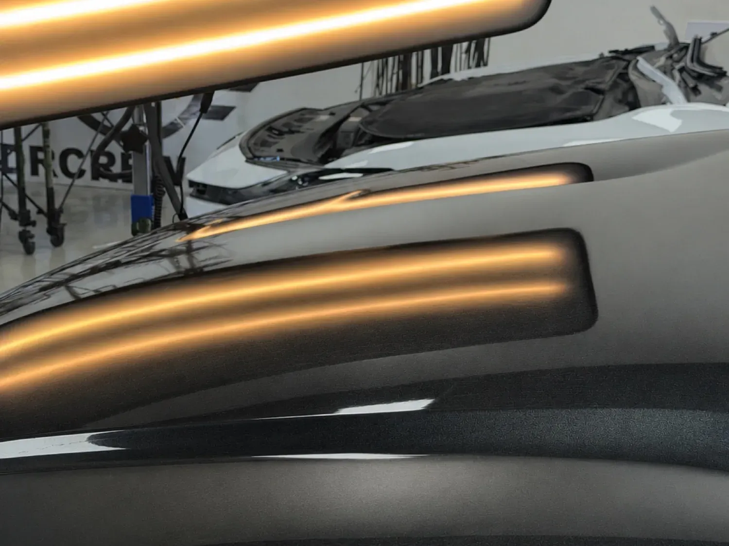 Black hood under a PDR line board, hail dents before and straight reflections after the repair — after