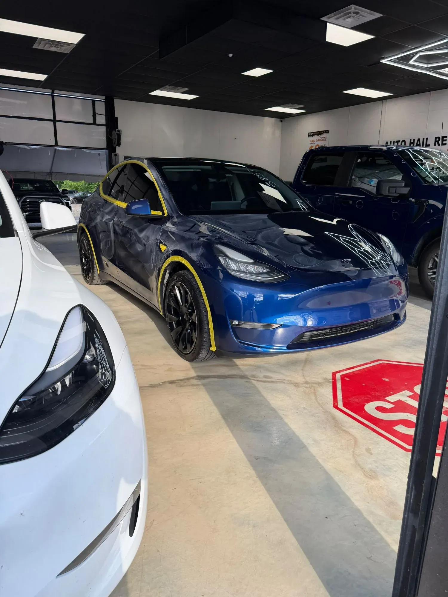 Blue Tesla Model Y in the shop with every hail dent circled in marker on the hood and doors