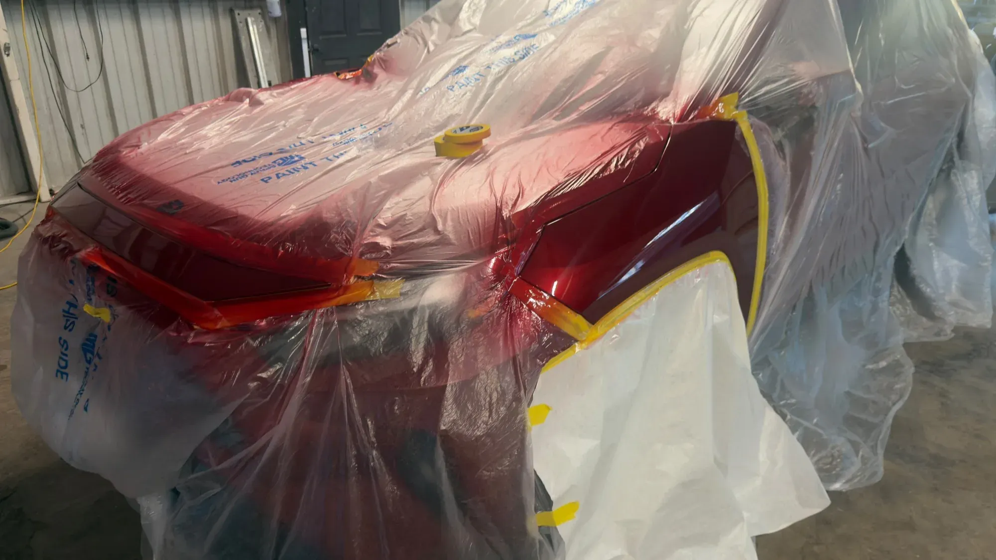 Red SUV rear end masked off in plastic and tape with fresh paint