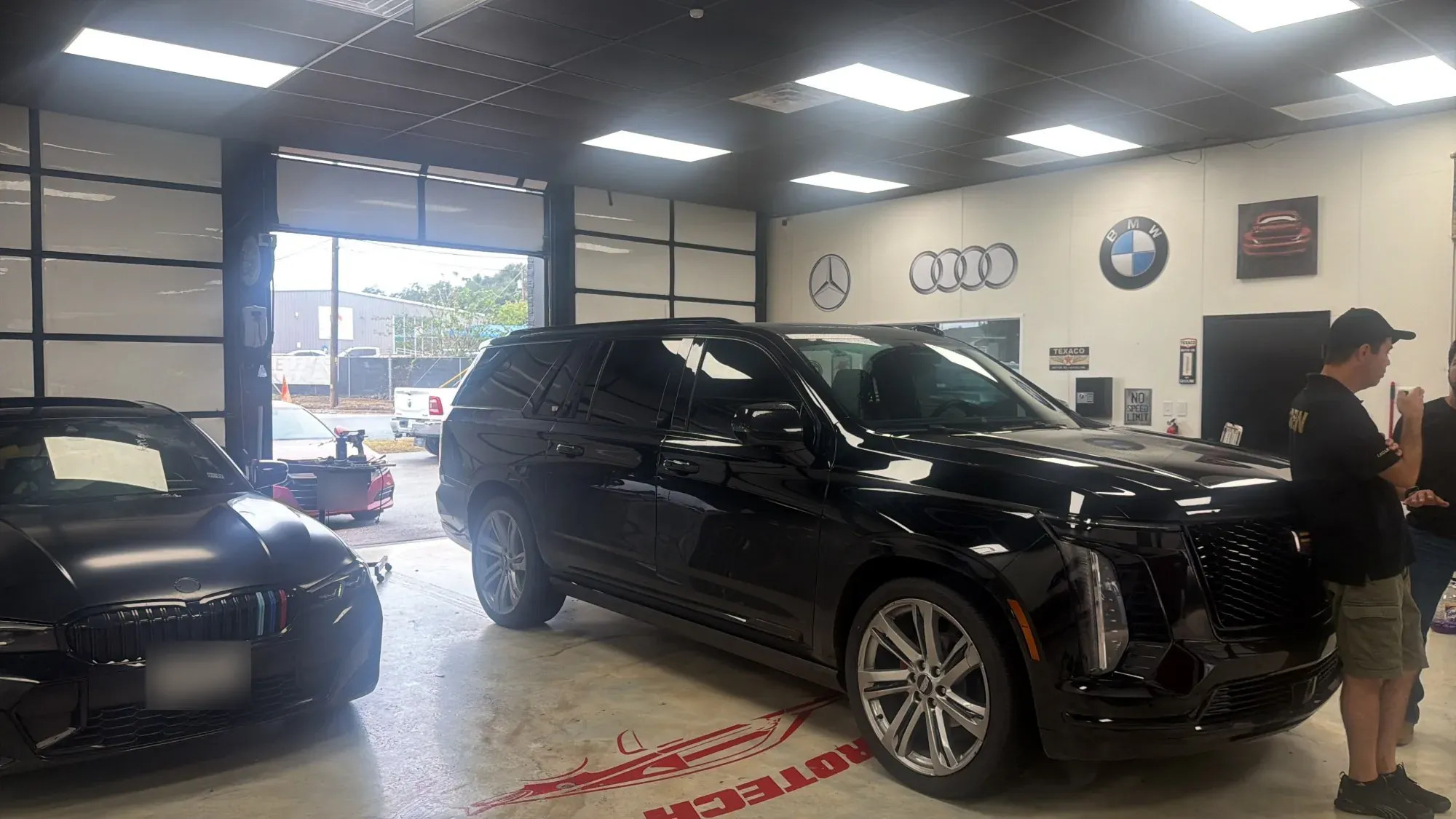 Cadillac Escalade and BMW in the PDR Crew shop with Mercedes, Audi and BMW logos on the wall